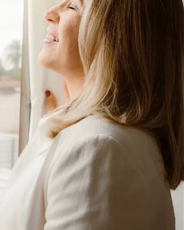 Mulher sorridente junto à janela, a desfrutar de bem-estar